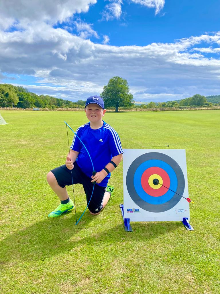A young boy is kneeling down next to a target in a field.