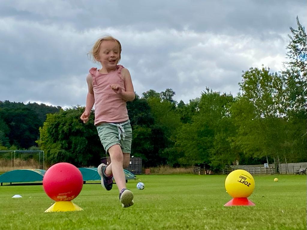 A little girl is running in a field with balls and cones