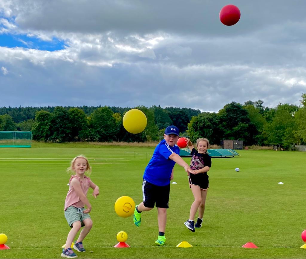A boy and two girls are playing with balls on a field.