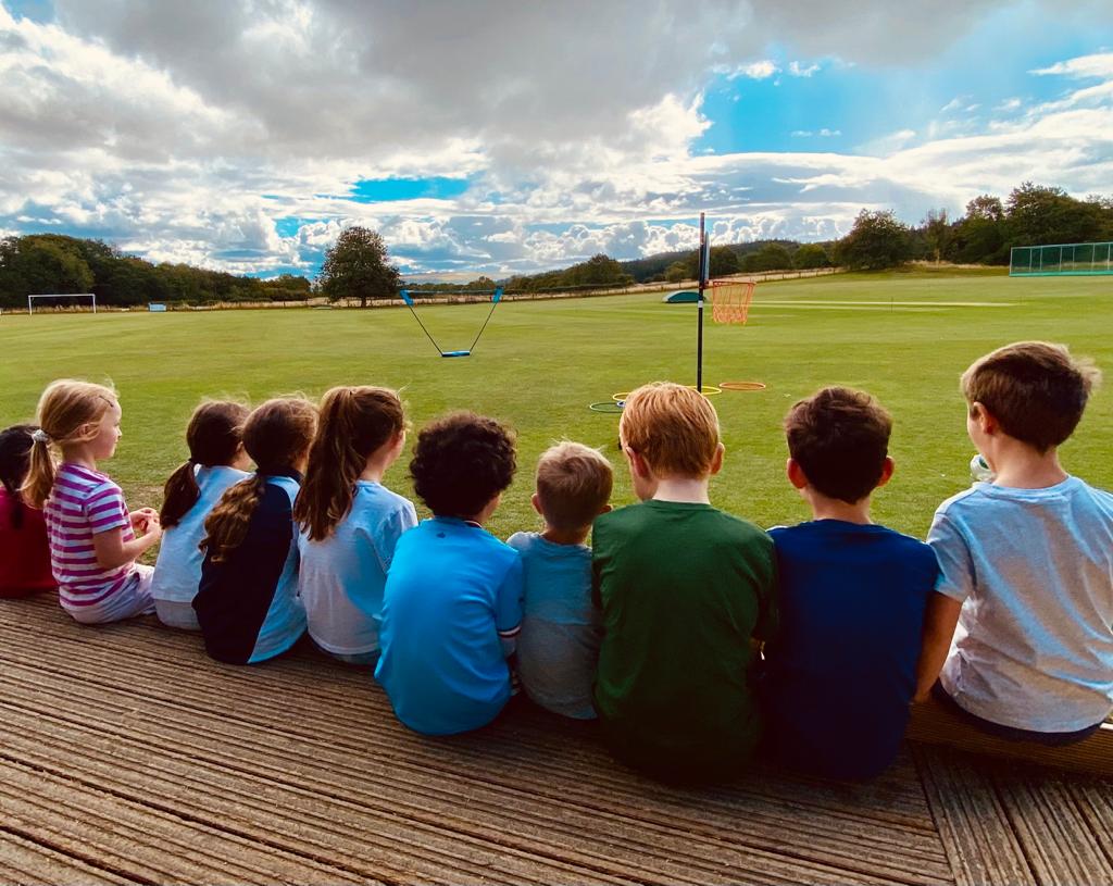 A group of children are sitting on a deck looking at a field.