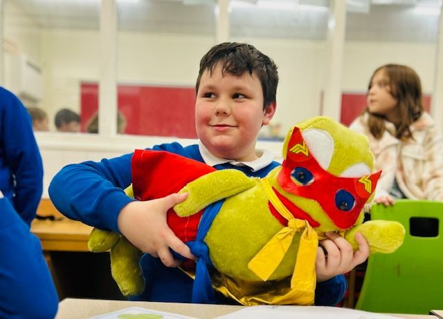 A boy is holding a stuffed animal in a superhero costume.