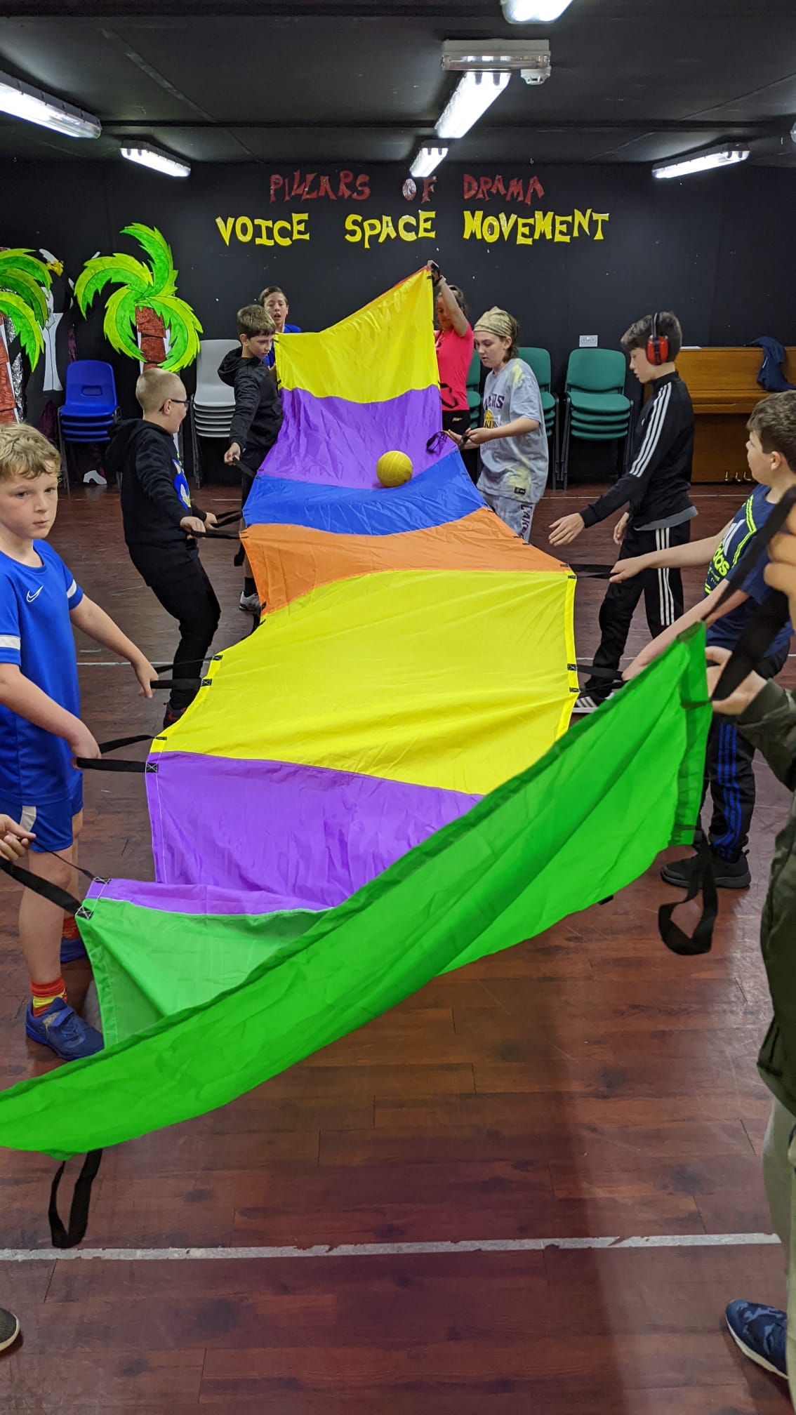 A group of children are playing with a colorful parachute in a gym.