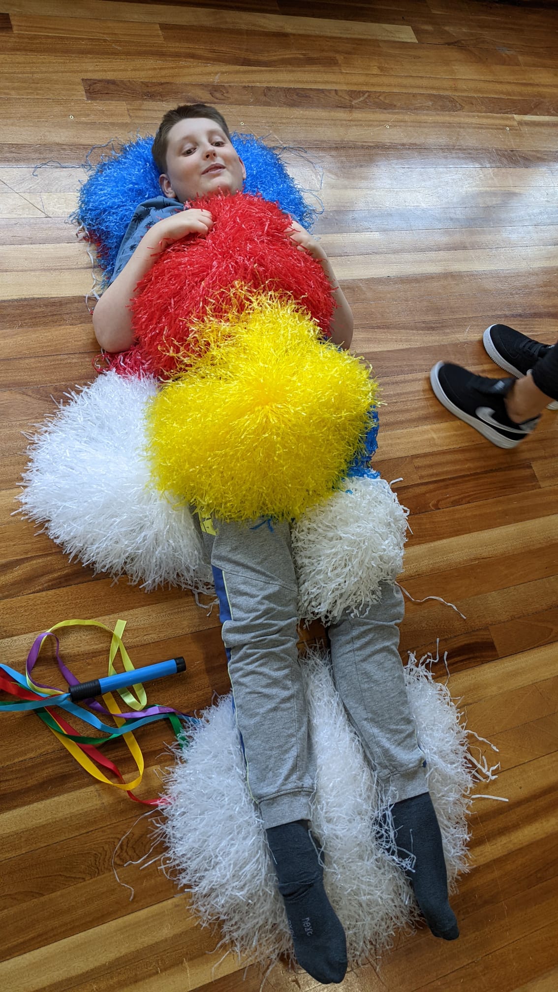 A young boy is laying on the floor covered in pom poms.