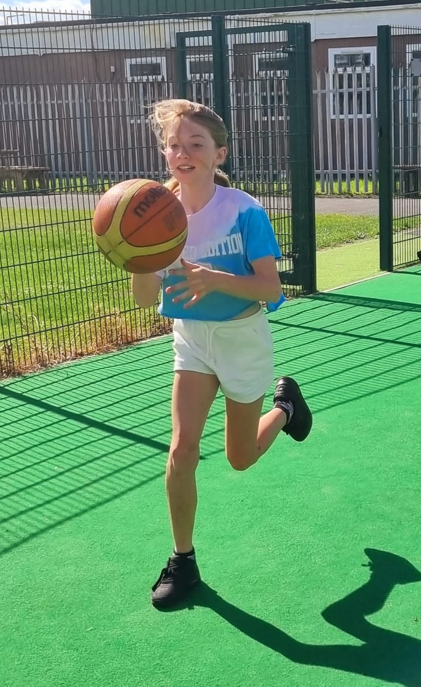 A young girl is running with a basketball on a court.