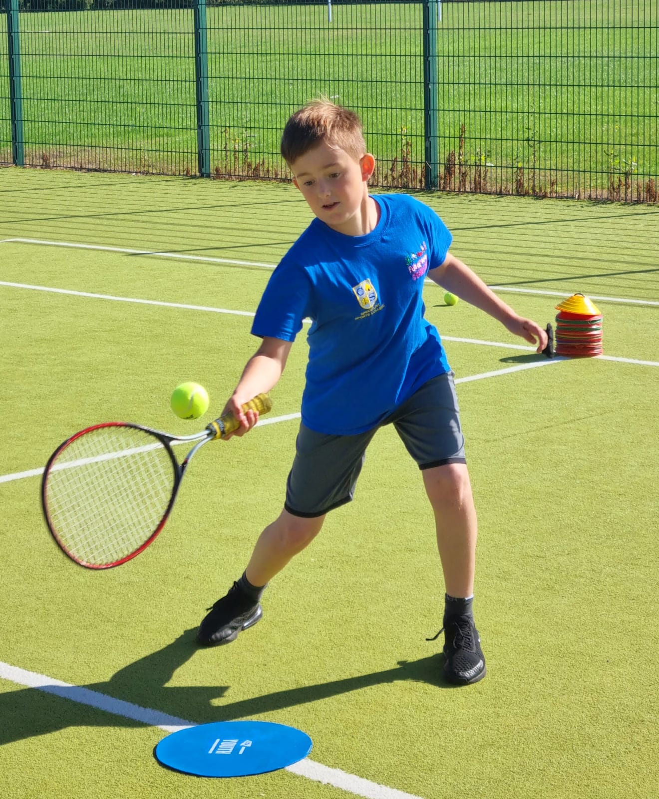 A young boy in a blue shirt is playing tennis