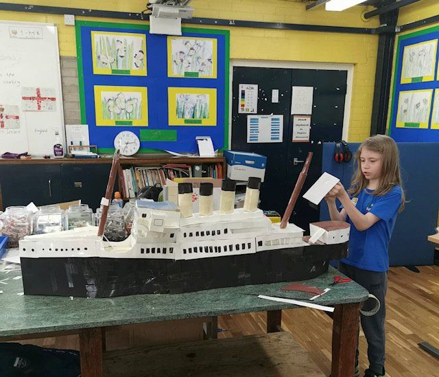 A little girl is standing in front of a model of the titanic