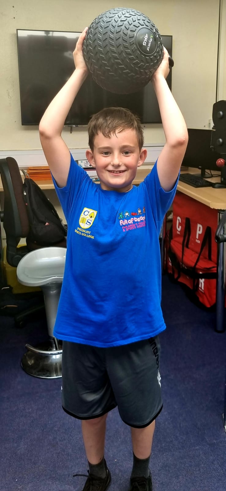 A boy in a blue shirt is holding a ball over his head.