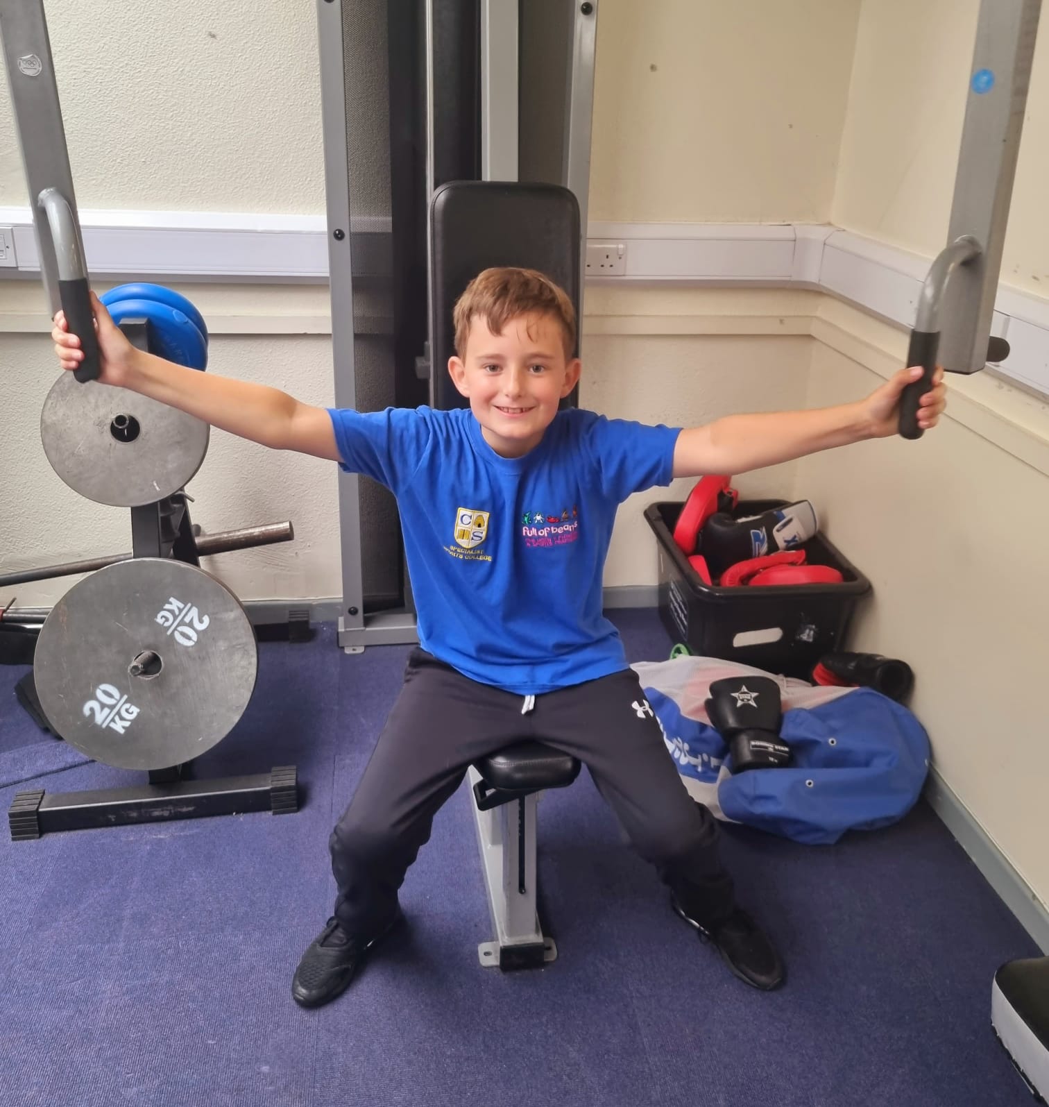 A young boy in a blue shirt is sitting on a bench in a gym