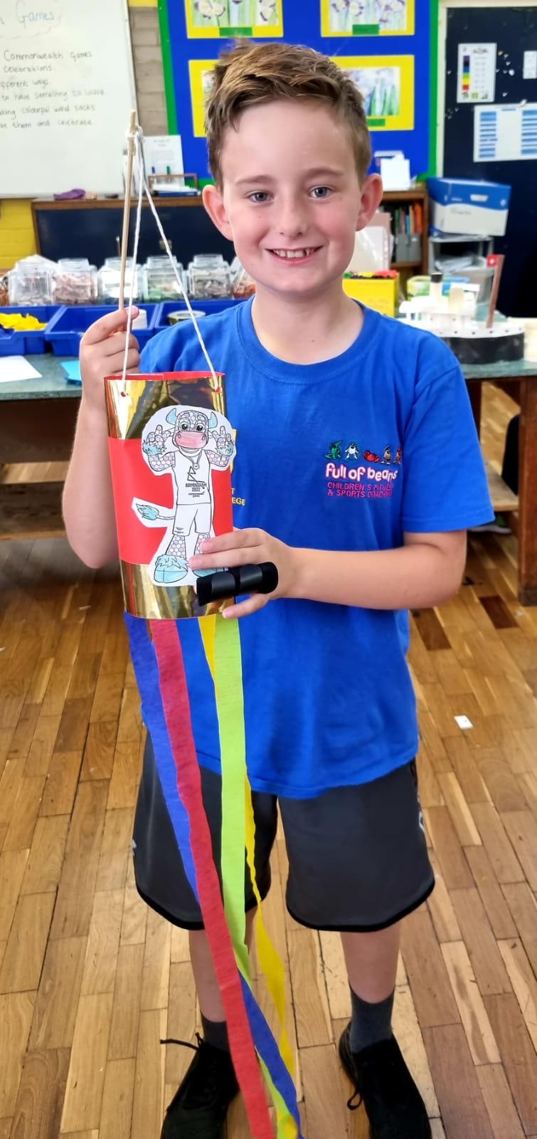 A young boy in a blue shirt is holding a kite in a classroom.