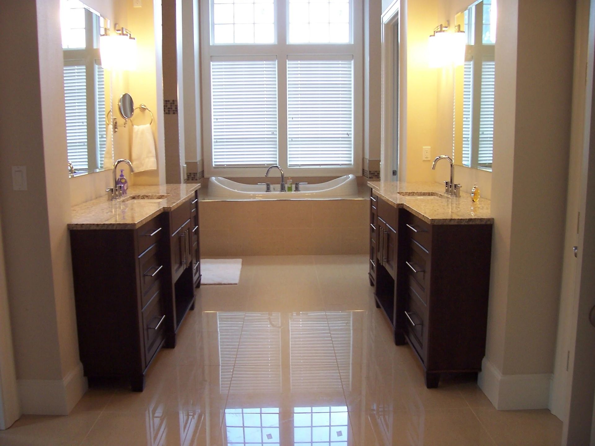 Elegant bathroom with dual vanities, bright windows, and glossy tiled floor
