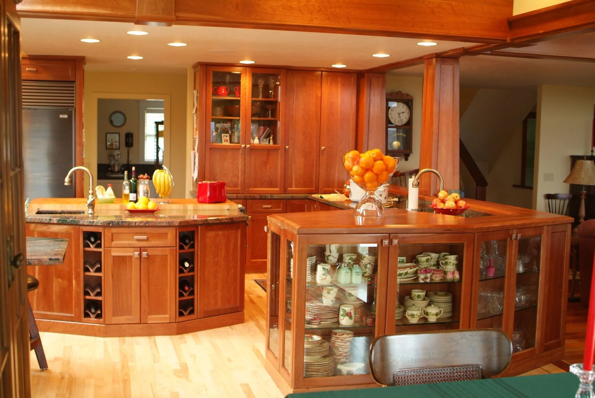 Wood-paneled kitchen with a central island, glass cabinets, and a bowl of oranges under warm lighting