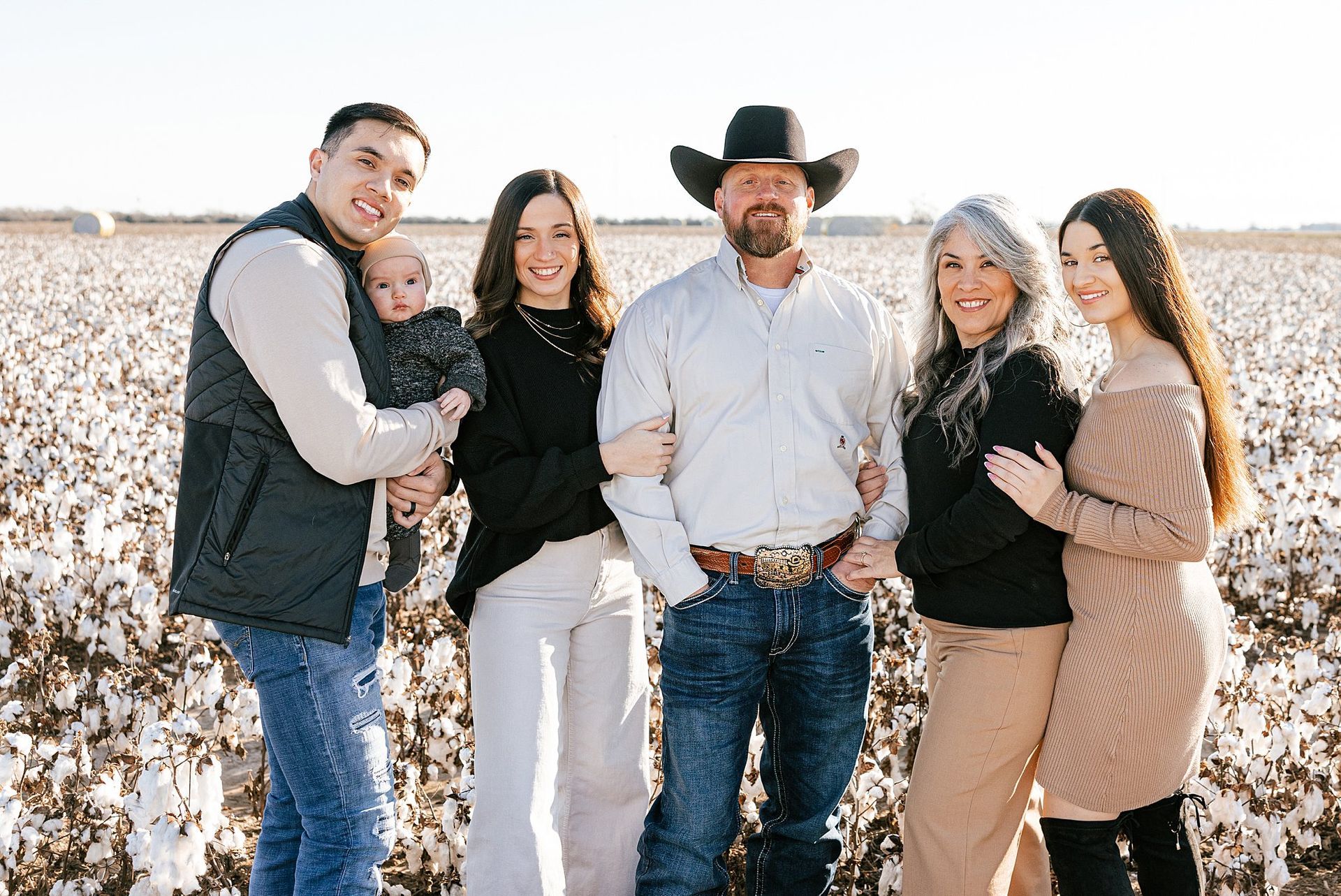 Family posing in a cotton field; man in cowboy hat, woman with silver hair, baby, teens, sunny day.