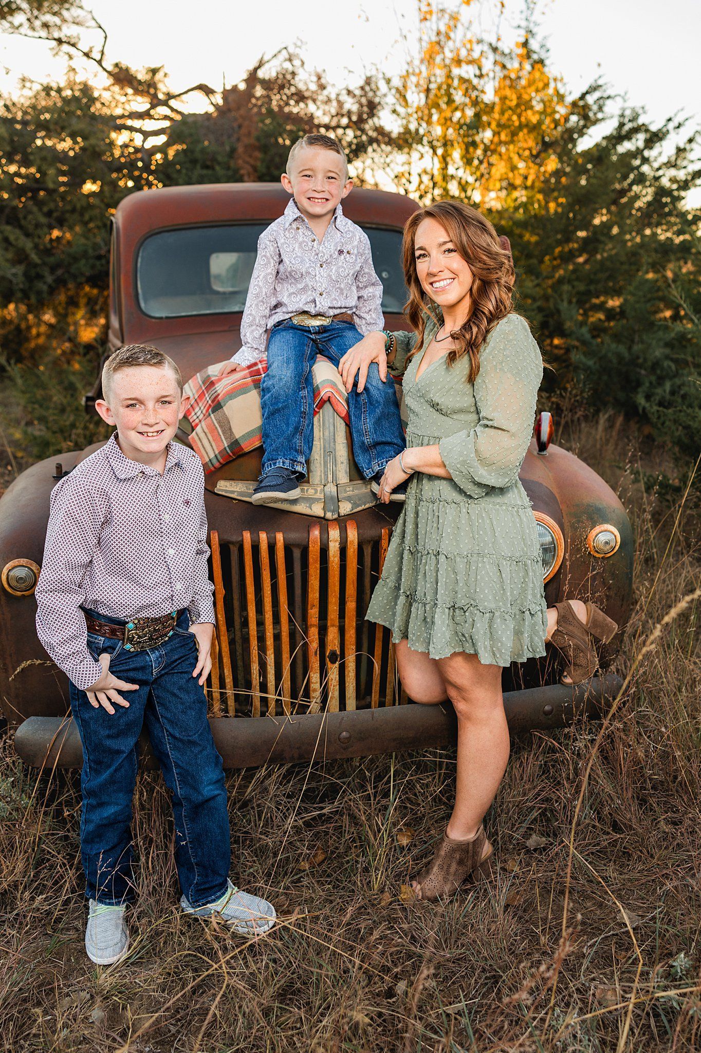 Family of three laughing on vintage pickup at sunset farm mini session in Burrton KS by Sara McMillian
