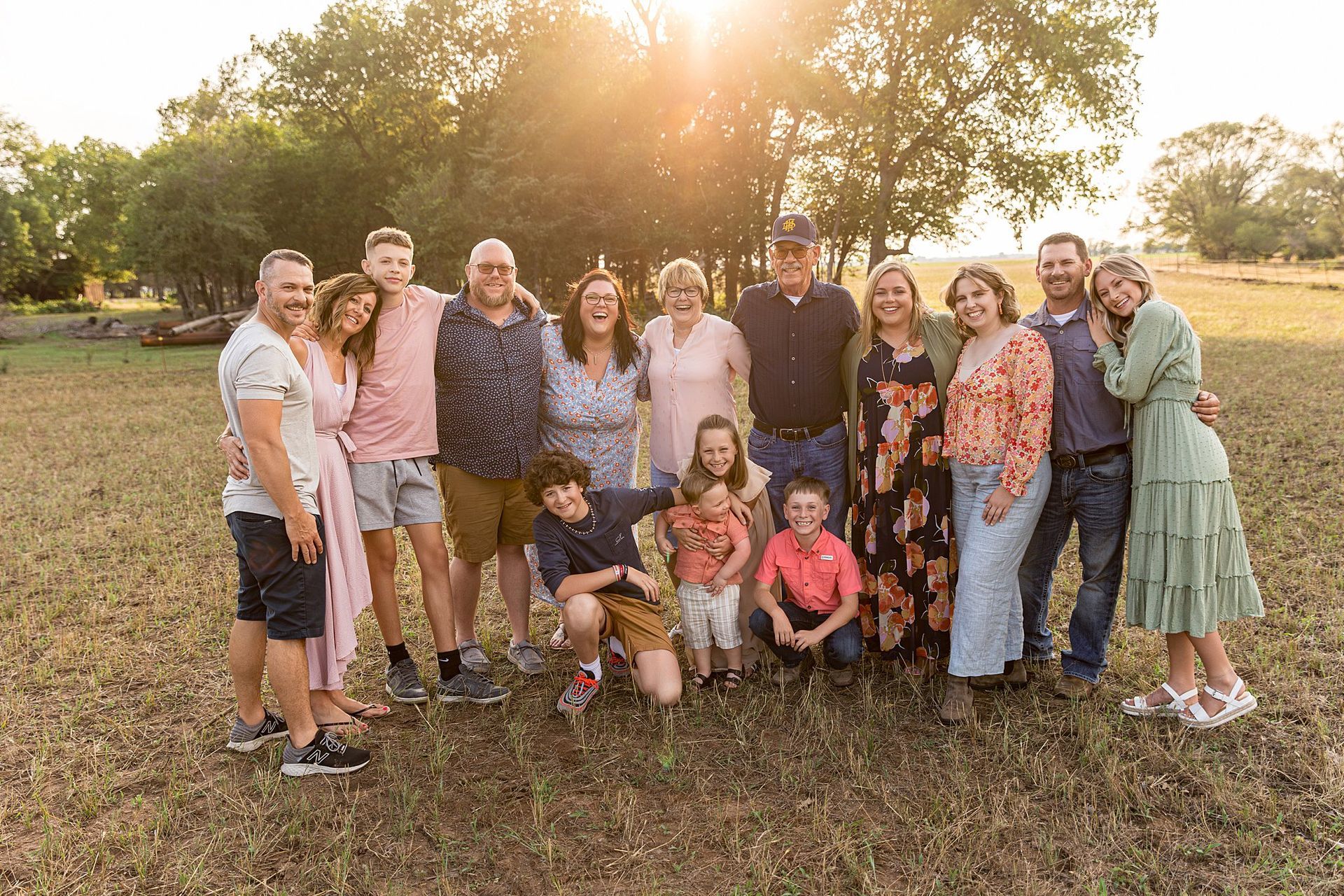 Family group portrait in a field at sunset; smiles, hugs, casual clothing.