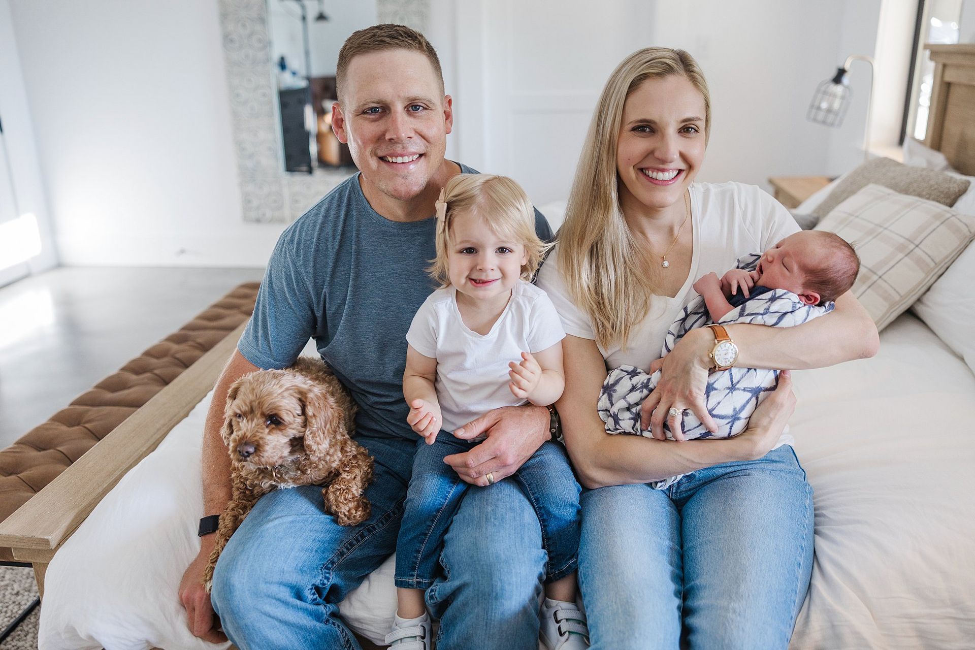 Candid family of four laughing around newborn in sunlit indoor session Haven KS photographer Sara McMillian