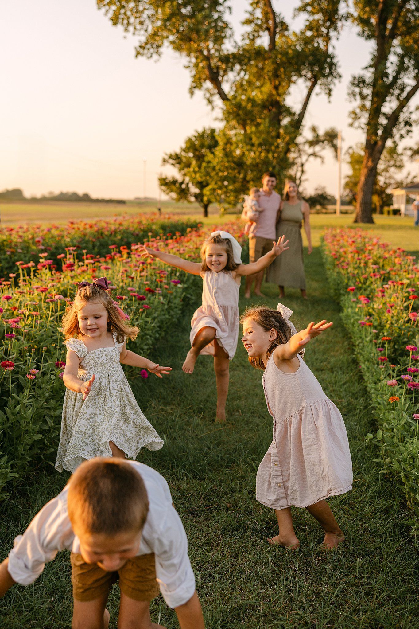 Children running and laughing in a flower field with parents in the background. Golden hour lighting.