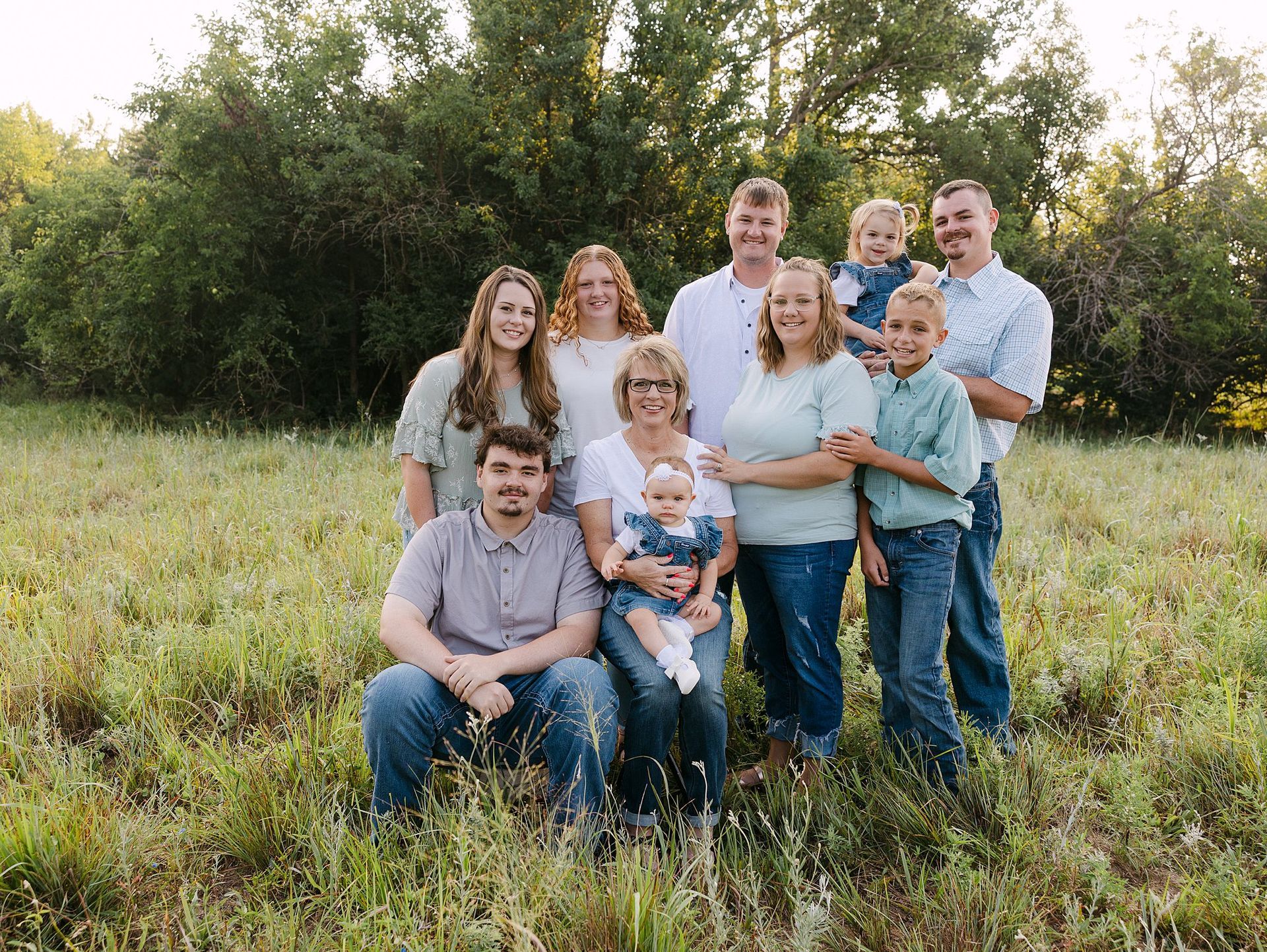 Family group poses in a field, smiling. People wear casual clothes, natural light.