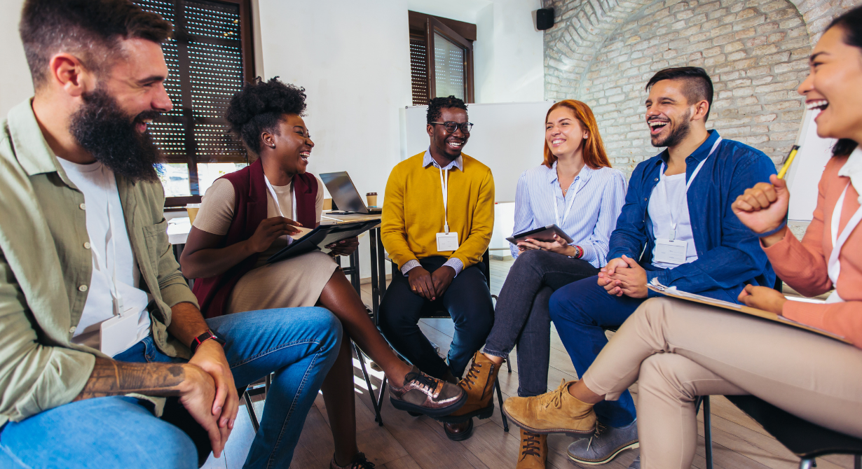 People seated in a bright room, smiling and talking in a group discussion.