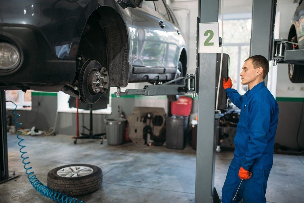 A Mechanic Works on A Car Lifted on A Hoist in A Garage — Woden Automotive Services in Phillip, ACT