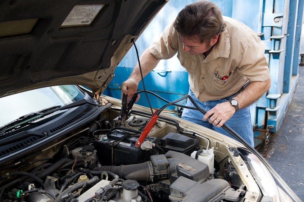 A Man Jumpstarting a Car Battery with Jumper Cables — Woden Automotive Services in Curtin, ACT