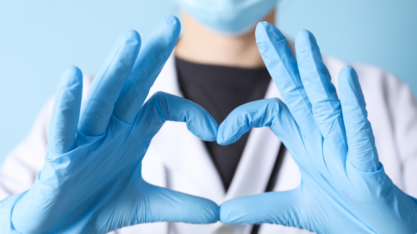Doctor in blue gloves and mask, making a heart shape with their hands.