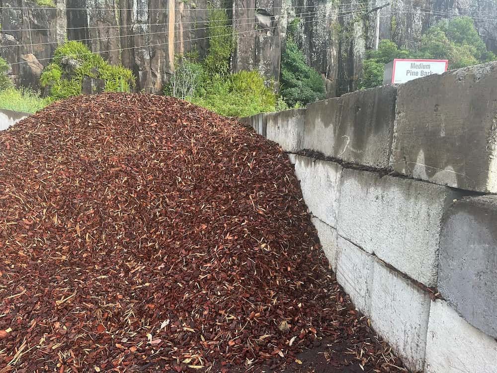 A Pile Of Mulch Is Sitting Next To A Concrete Wall — Burnetts On Barney in Berry, NSW