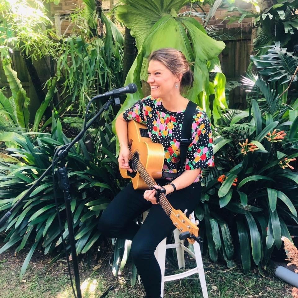 A Woman Is Sitting On A Stool Playing A Guitar In Front Of A Microphone — Burnetts On Barney in Kiama, NSW