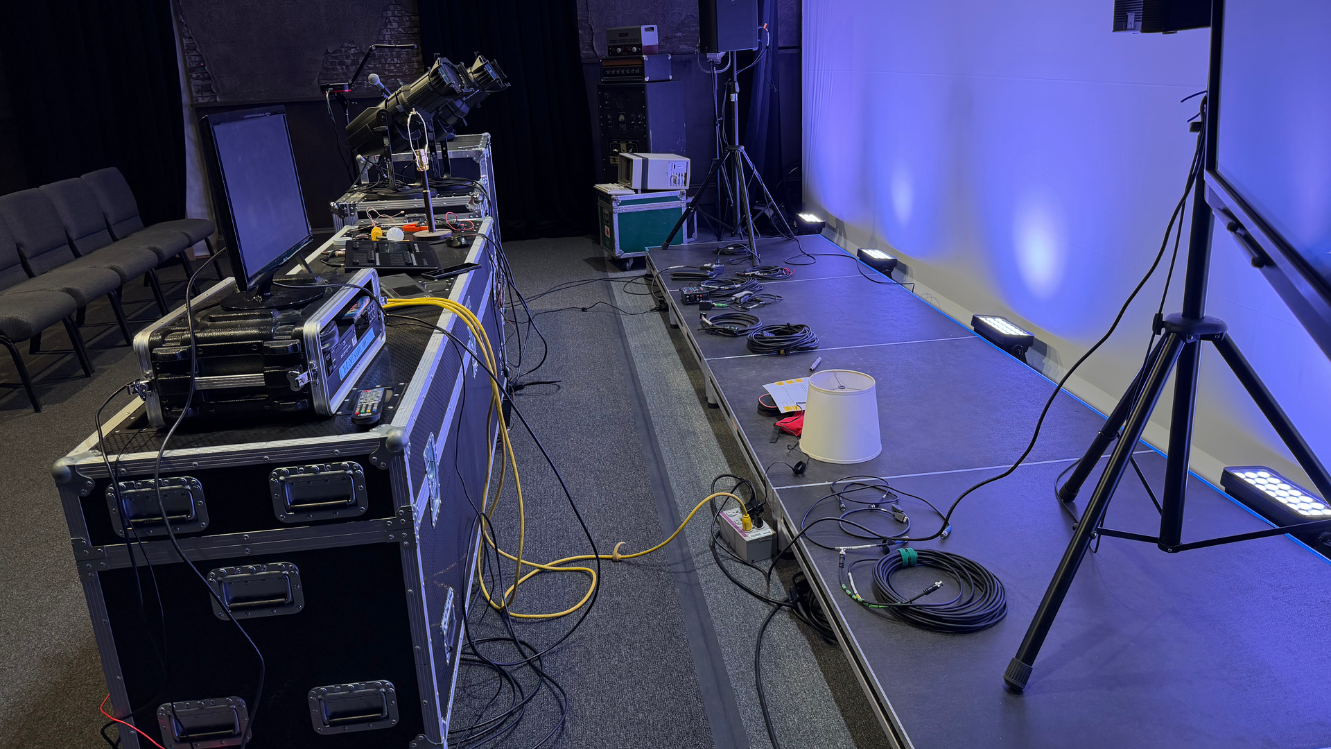 Stage setup with equipment, lights, and cables. Dark interior with blue wall lighting.