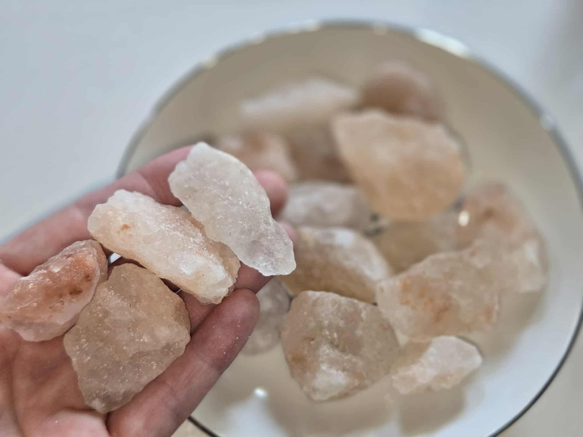 Pink Himalayan salt chunks in a white bowl with a silver rim.