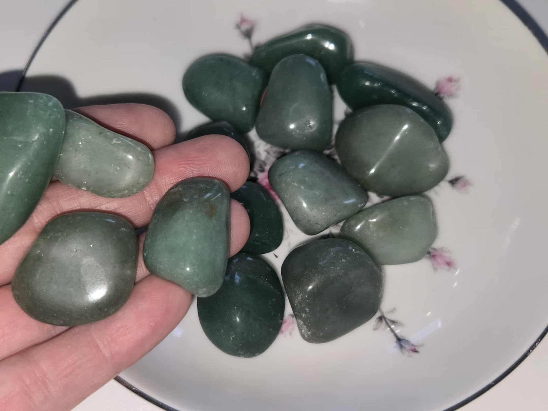 Green tumbled stones in a white bowl with floral details.