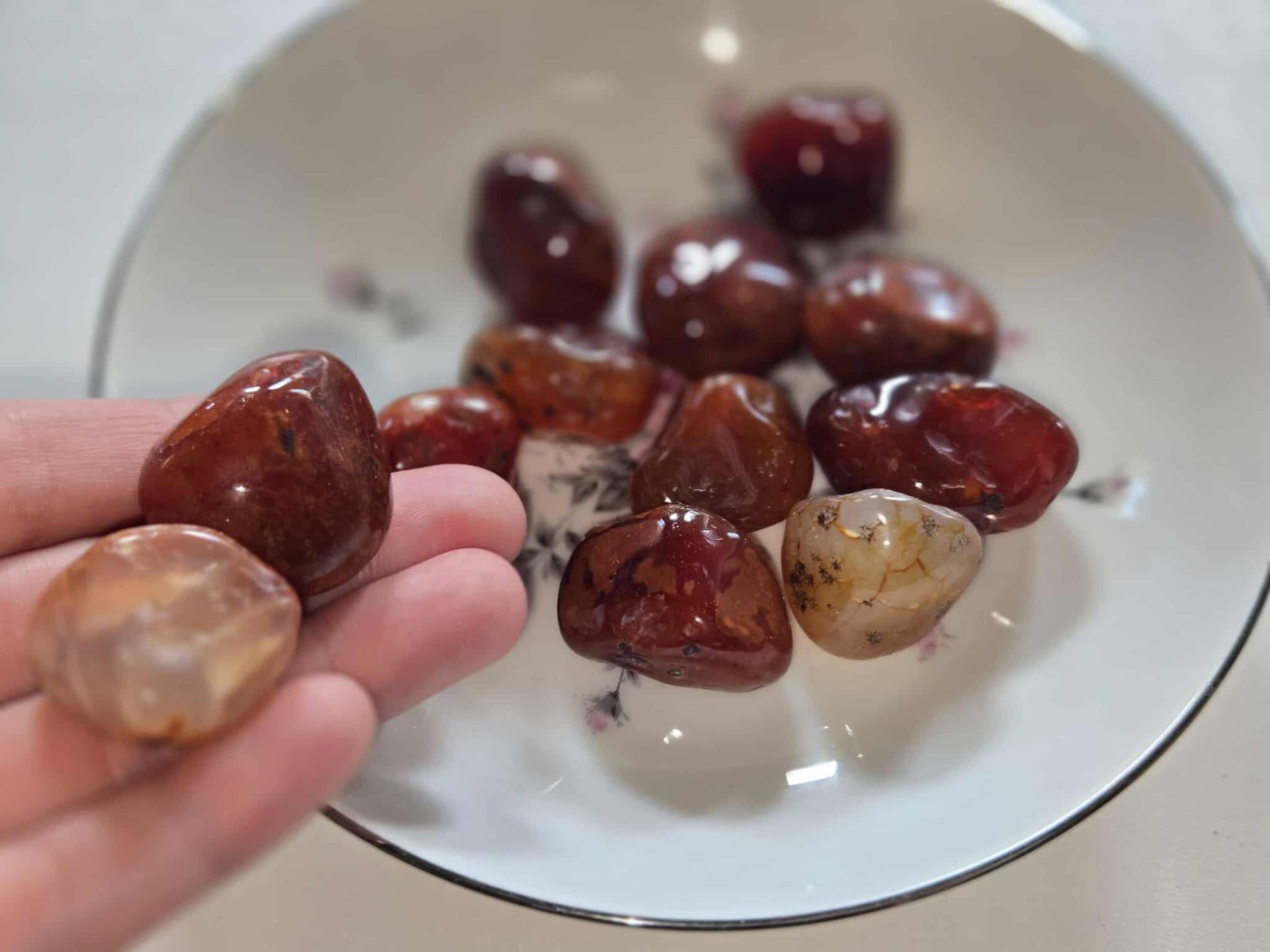 Red-brown polished stones in a white floral dish on a white surface.