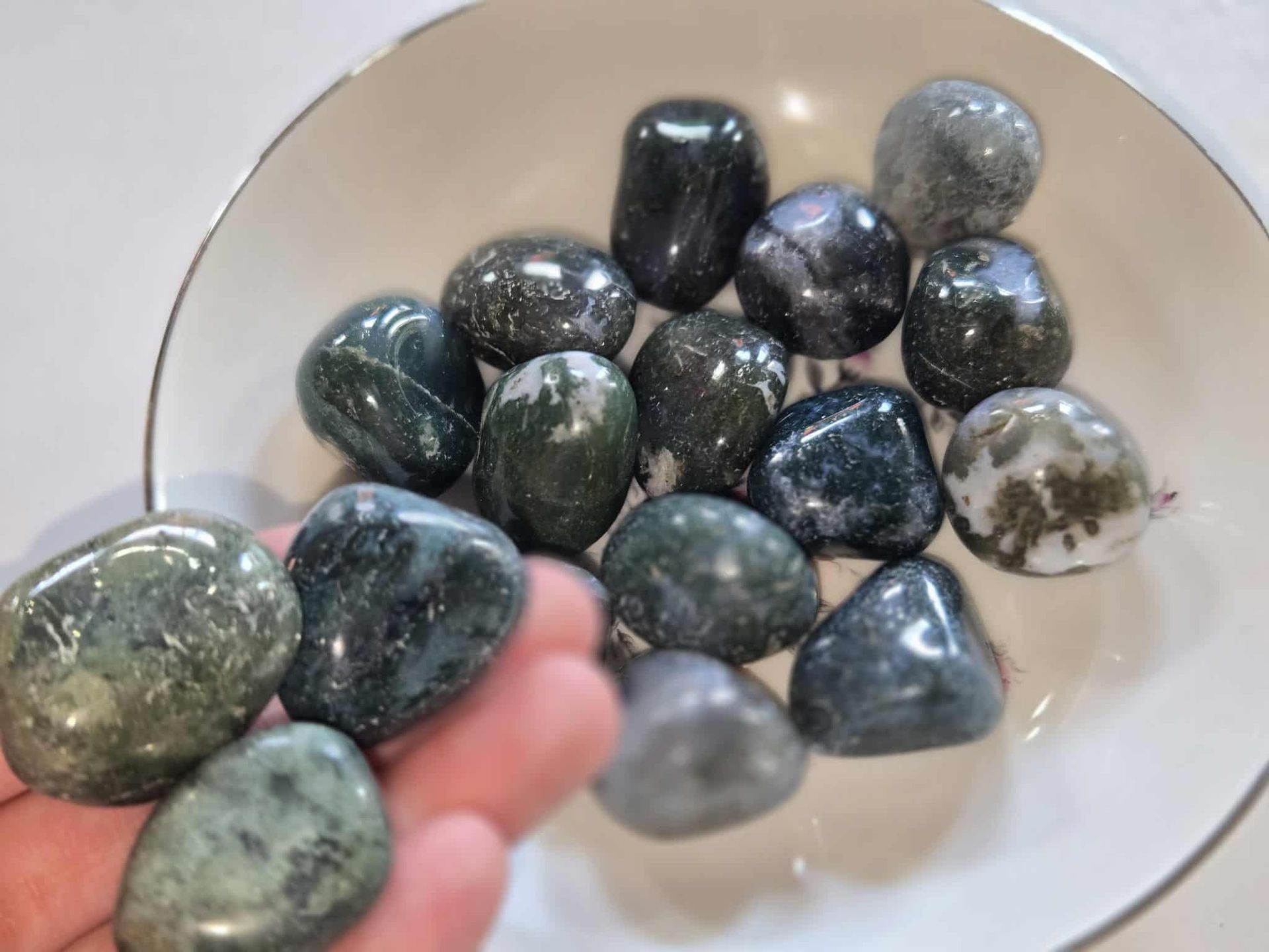 A white bowl filled with a collection of smooth, dark green and grey tumbled stones.