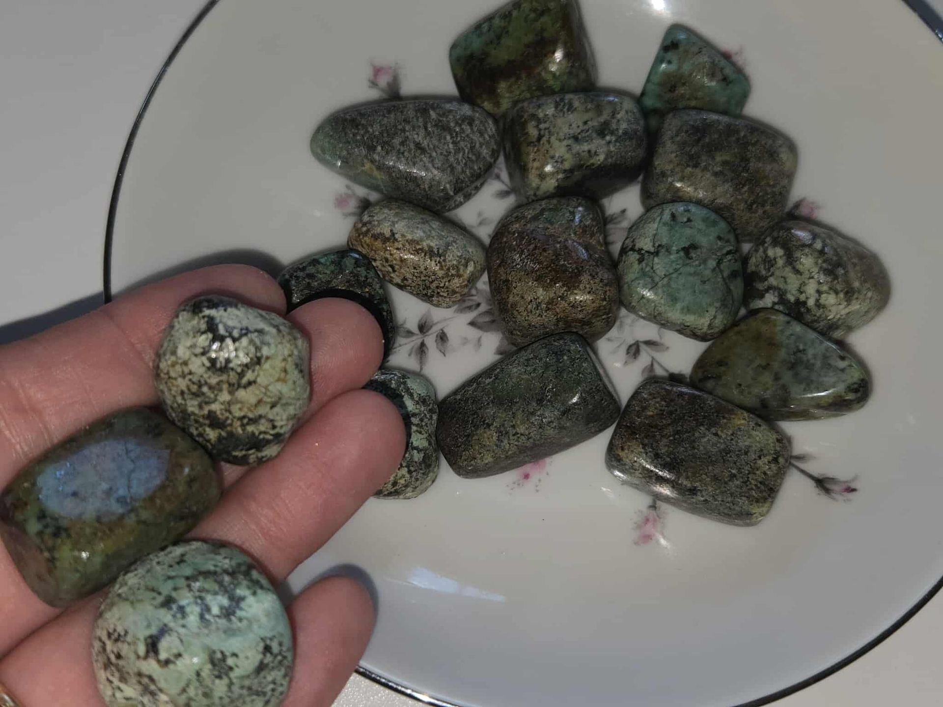 Tumbled turquoise-colored stones in a white floral-decorated dish with a silver rim.