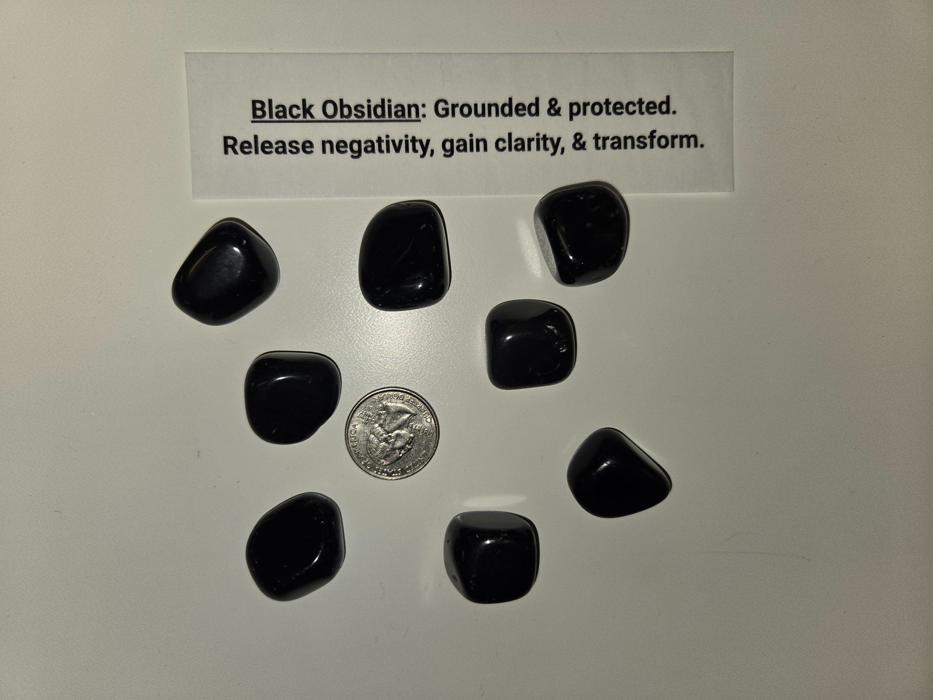 A group of black obsidian stones are displayed on a white surface