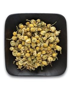 A black bowl filled with dried chamomile flowers on a white background.