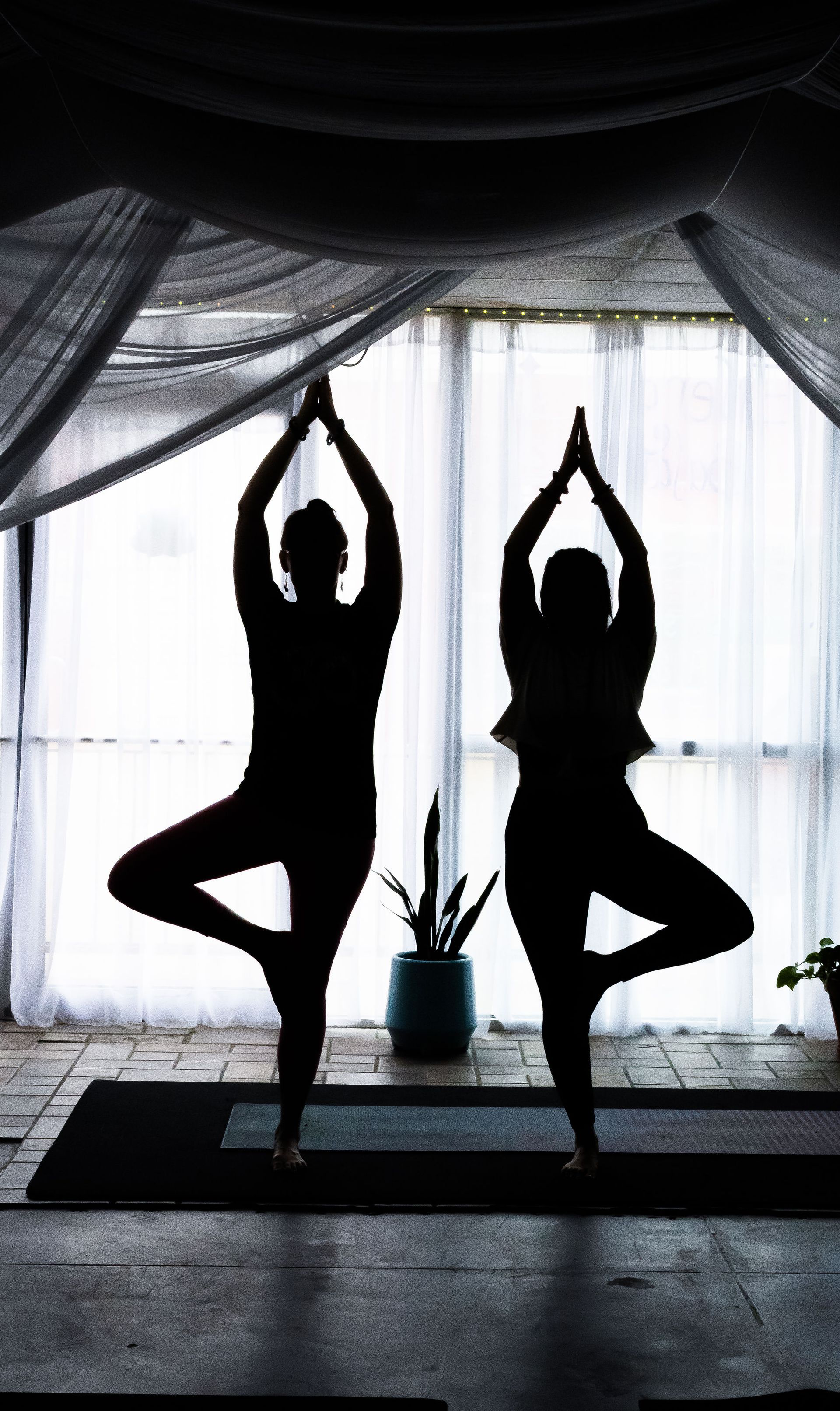 Silhouettes of two people doing yoga in front of a window