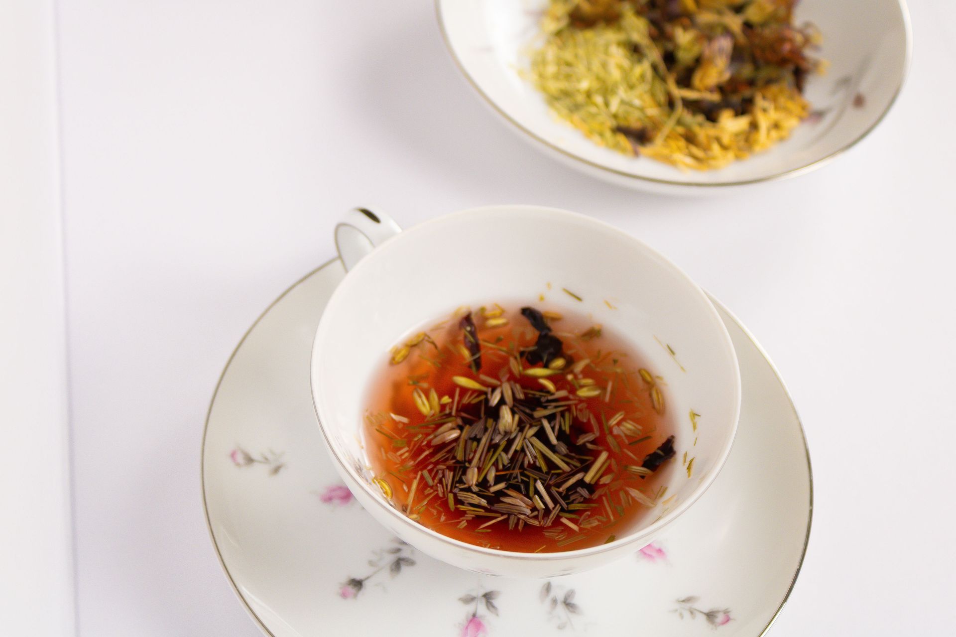 A cup of tea sits on a saucer next to a bowl of tea leaves