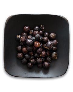 A black bowl filled with juniper berries on a white background.