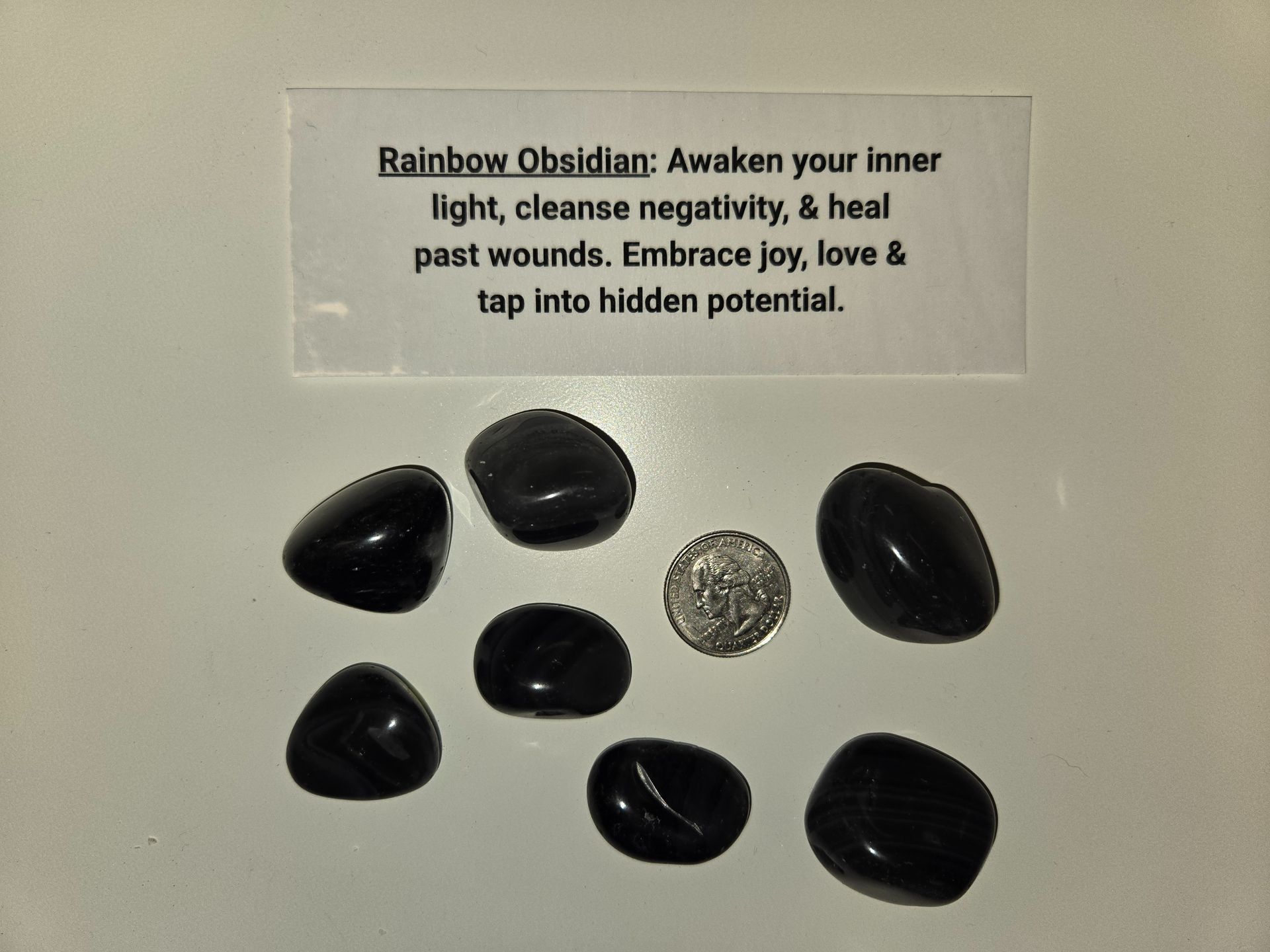A pile of black stones next to a card that says rainbow obsidian