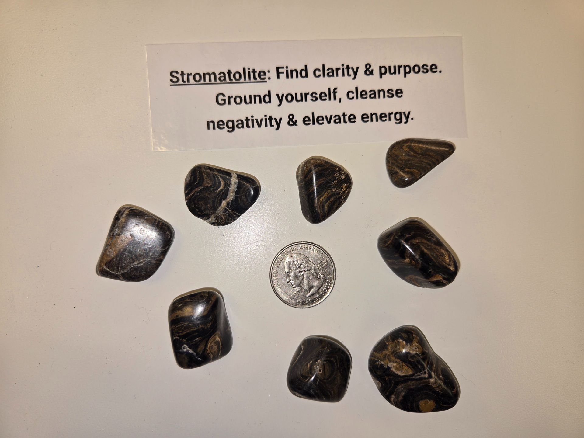 A group of black stones with a card that says stromatolite find clarity & purpose ground yourself cleanse negativity & elevate energy