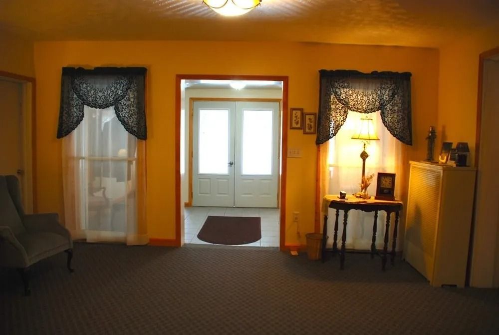Living room with two doorways, yellow walls, dark curtains, and a table with a lamp.