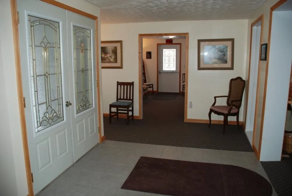 Hallway with ornate doors, two chairs, paintings, and a door leading outside.