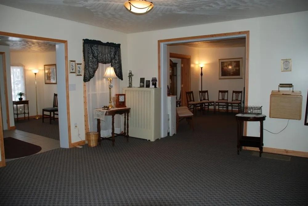 Interior of a funeral home with open doorways to other rooms, carpeted floors, and a small table with a lamp.