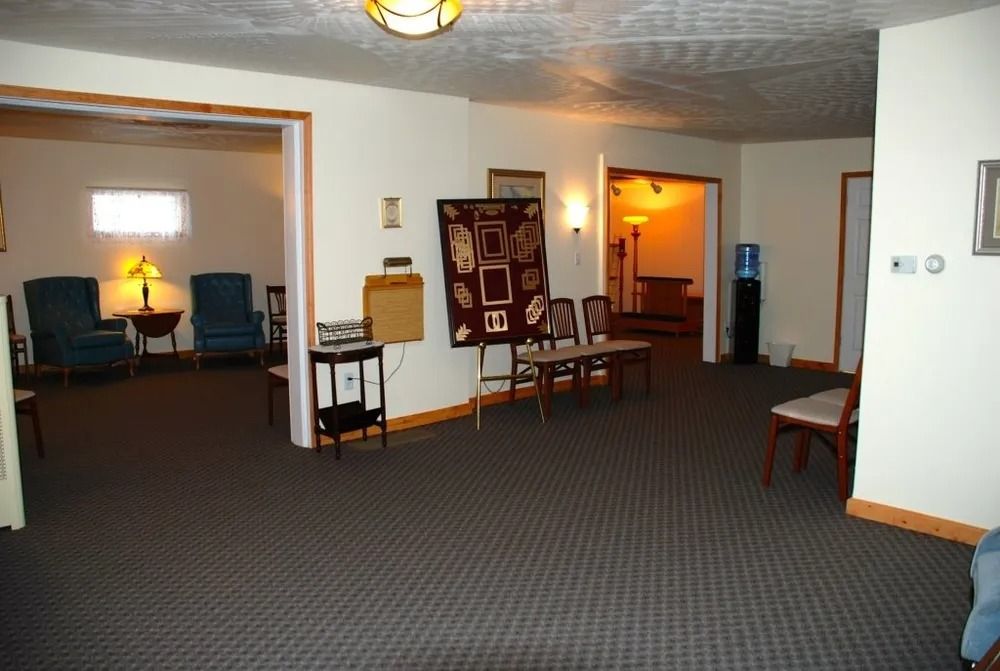 Interior of a sparsely furnished waiting room with dark carpet, neutral walls, and doorways leading to other rooms.