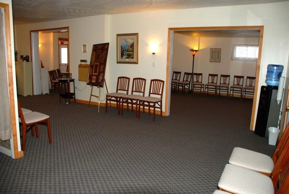 A funeral home waiting room with chairs, carpet, artwork, and water dispenser.