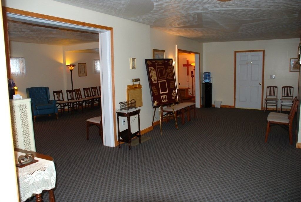 Interior of a funeral home with chairs, a casket display, and doorways.