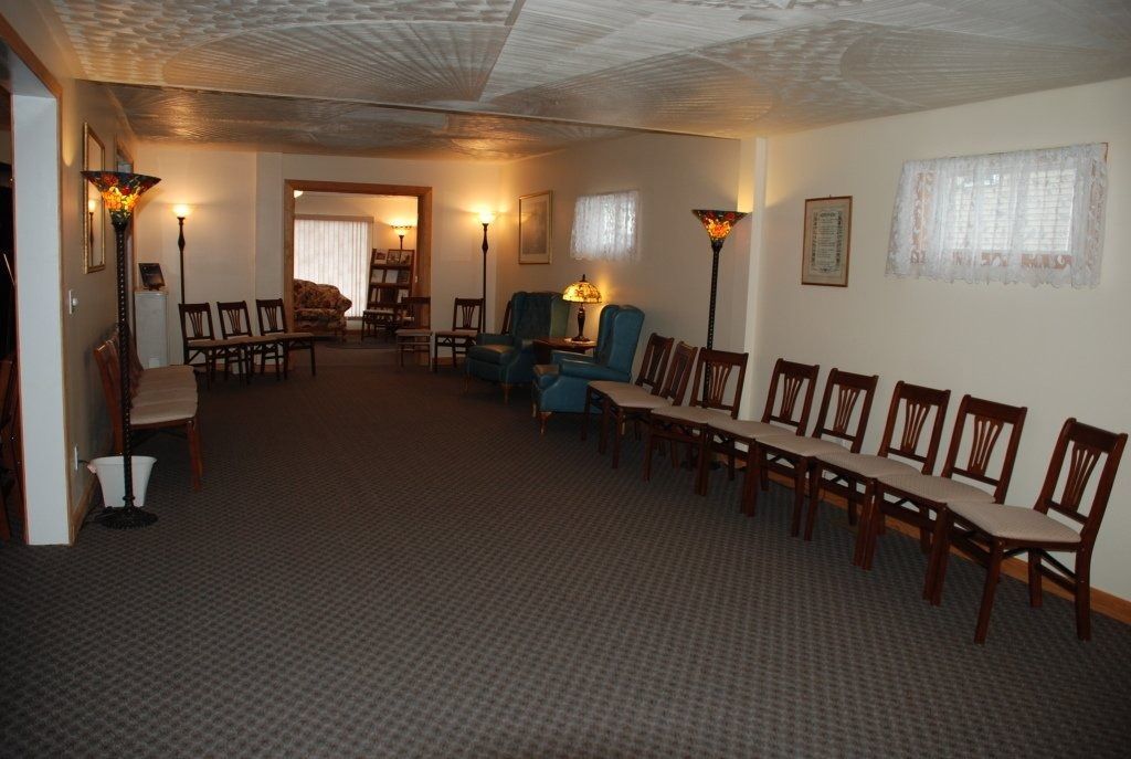 A waiting room with chairs, lamps, and a patterned carpet; a doorway leads to another room.