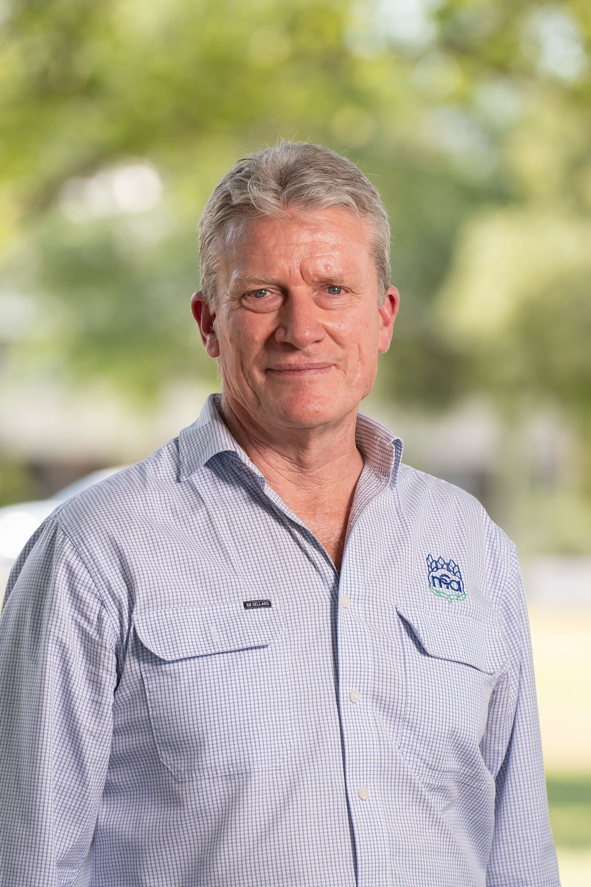 Man in blue button-down shirt smiling outdoors, light background.