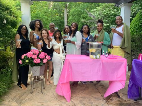 A group of people are standing around a table with a pink table cloth.