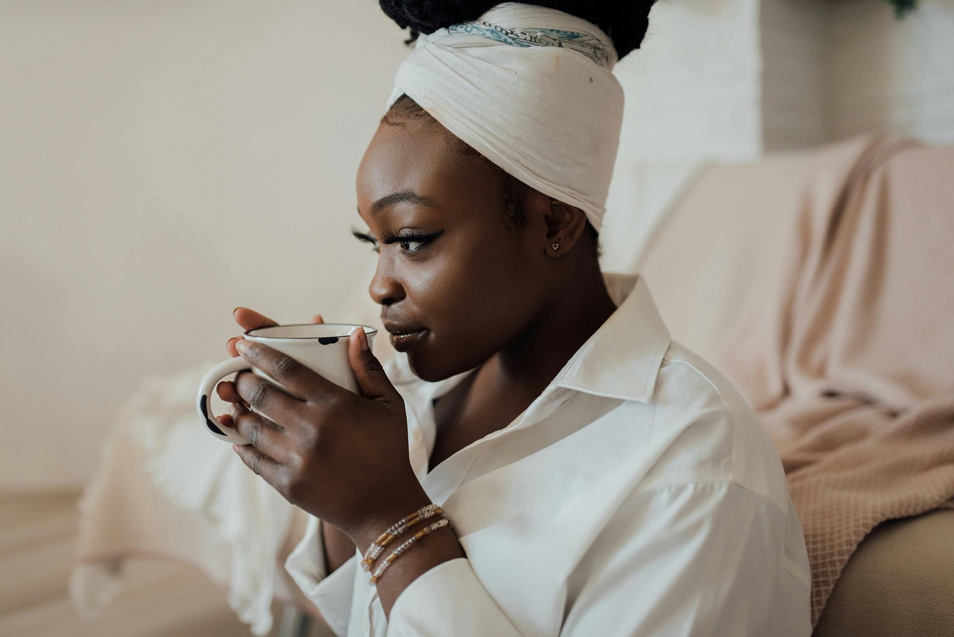 A woman is sitting on a couch drinking a cup of coffee.